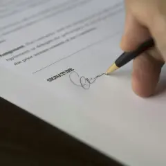 Dłoń podpisuje dokument. Warto wiedzieć, jakie schorzenia skutkują nieważnością testamentu, by uniknąć problemów prawnych.