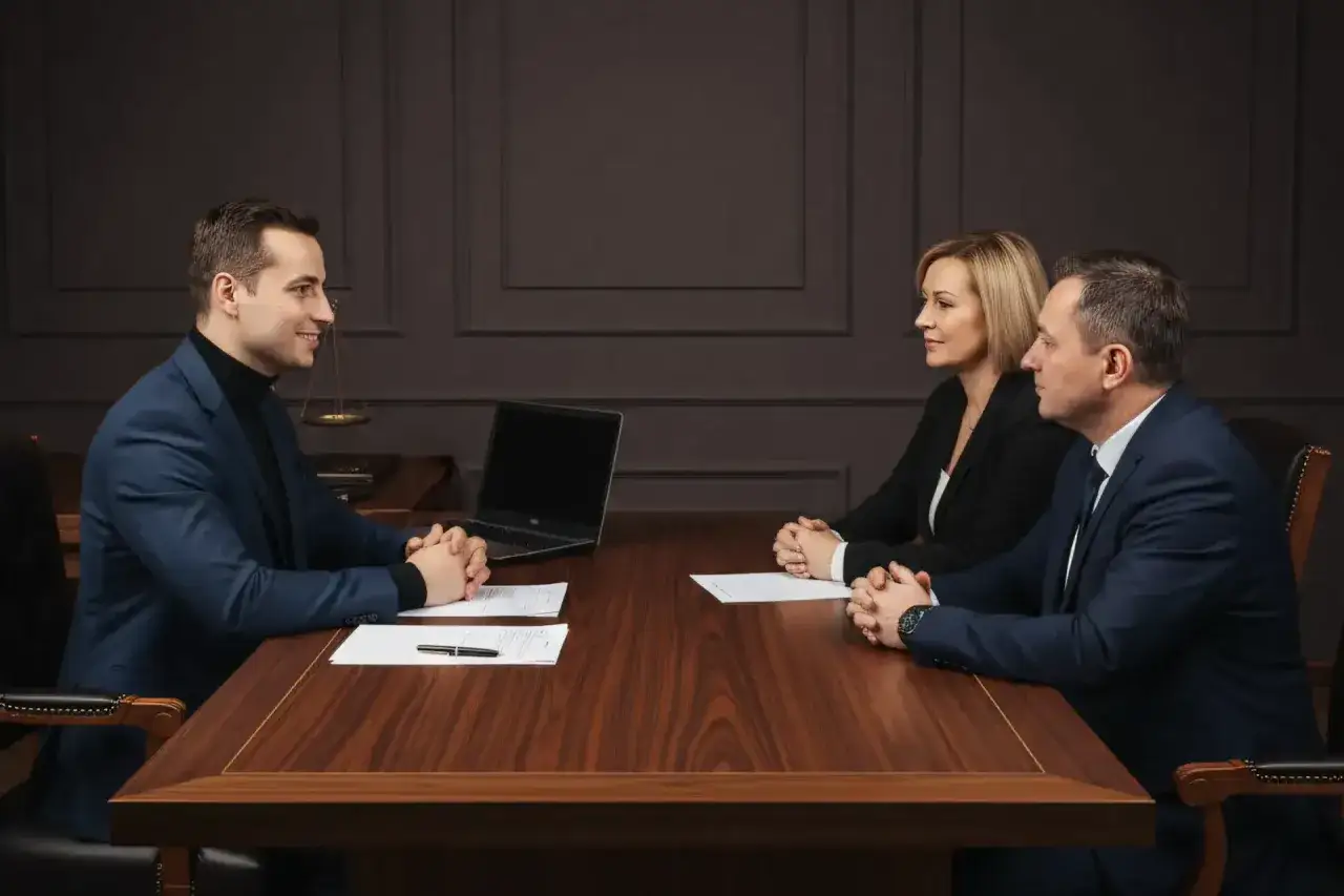 Trzy osoby przy stole omawiają sprzedaż mieszkania a spłatę dzieci. Prawnik, kobieta i mężczyzna dyskutują nad dokumentami.
