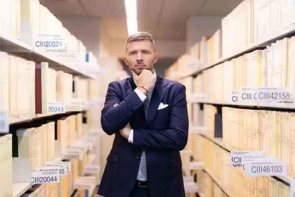 Mężczyzna w garniturze zastanawia się, jak liczyć 6 miesięcy na odrzucenie spadku, wśród regałów pełnych akt.